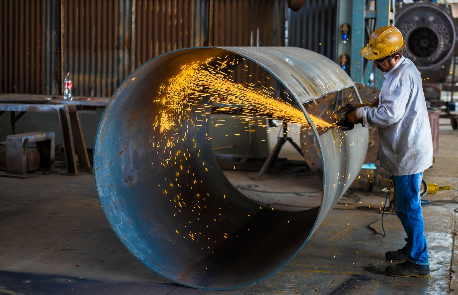 Metalworker in yellow hard hat operating an angle grinder
